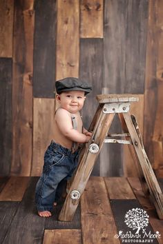 a baby boy in overalls and a hat standing on a wooden steplade