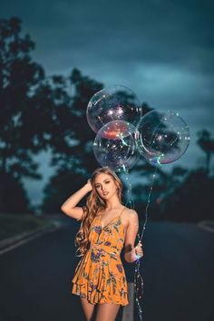 a woman in an orange dress is holding two large bubbles and posing for the camera