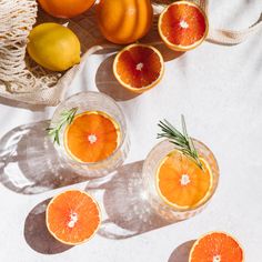 oranges, lemons and rosemary are arranged in glass bowls on a white surface