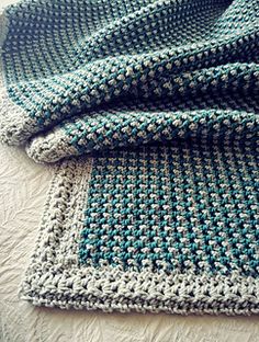 a crocheted blanket laying on top of a bed next to a white pillow