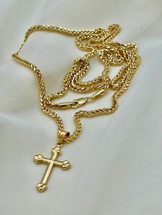 a gold cross necklace is laying on a white cloth with a chain attached to it