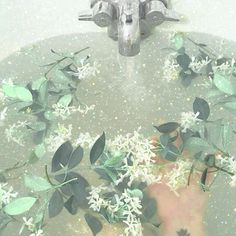 a person's hand is in the water with flowers and leaves floating on it