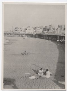 an old black and white photo of people on the beach with buildings in the background