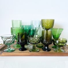 a wooden tray topped with lots of different colored glass bowls and glasses on top of each other