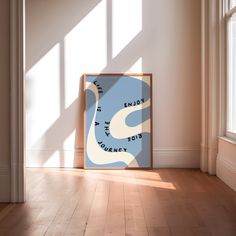 a framed poster sitting on top of a hard wood floor in an empty room with sunlight coming through the windows