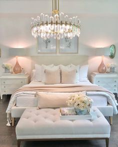 a white bedroom with chandelier above the bed and pillows on the foot board