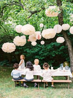 a group of children sitting at a picnic table with paper lanterns hanging from the trees