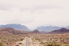 an empty road in the middle of desert with mountains in the backgrouds