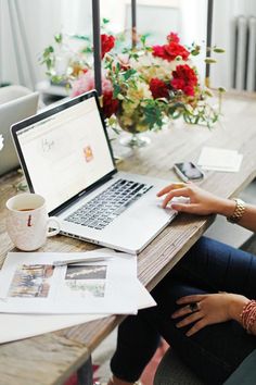 a woman sitting at a table with a laptop computer on her lap and coffee mug in front of her