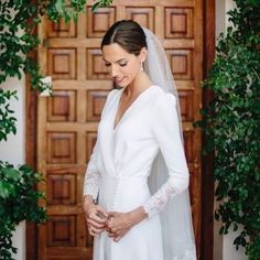 a woman in a white wedding dress standing next to a wooden door wearing a veil