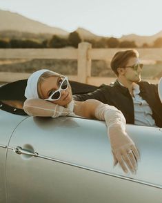 a man and woman sitting in the back of a silver car with sun glasses on