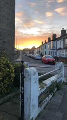 cars are parked on the street in front of some houses at sunset or sunrise time