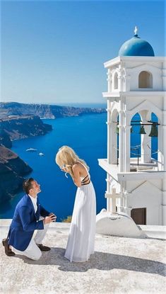 a man kneeling down next to a woman on top of a hill near the ocean