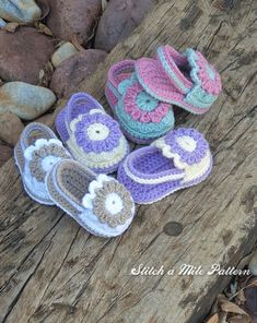 three crocheted baby shoes sitting on top of a wooden log next to rocks