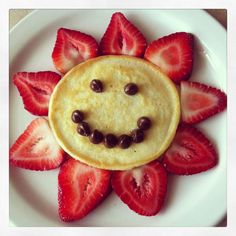 a smiley face made out of strawberries on a white plate with chocolate chips in the shape of a sunflower