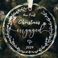 a glass ornament hanging from a christmas tree with the words, our first christmas engaged