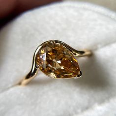 a fancy yellow diamond ring sitting on top of a white cloth covered cushioned surface