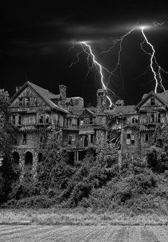 black and white photograph of an old abandoned house with lightning in the sky above it