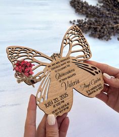 a person holding up a wooden butterfly shaped wedding card with flowers in the center and words on it