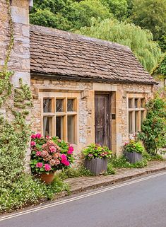 an old stone building with flowers growing on the side of it's windows and door