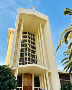 a tall white building with a cross on it's side and palm trees in front