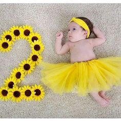 a baby wearing a yellow tutu laying on the floor next to sunflowers