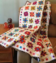 a quilted blanket sitting on top of a chair next to a table with a vase