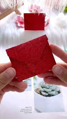 a person is holding an envelope with red paper in front of some other items on a table