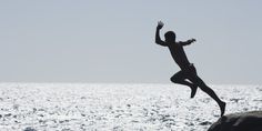 a man is jumping into the air from a rock in front of some water and rocks