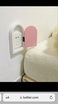 a white bed with a pink headboard on top of it and a light switch attached to the wall