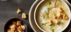 a bowl of soup with tofu and broccoli in it next to a small bowl of crackers