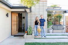 a man and woman standing in front of a house with a dog on their lap