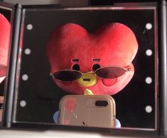 a red teddy bear wearing sunglasses and holding a cell phone in front of two mirrors