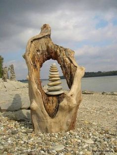 a rock stack sitting on top of a tree stump next to the water and rocks