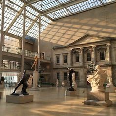 the inside of a museum with statues and glass ceilinged area for people to look at