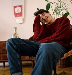 a man sitting in a wicker chair with his hand on his head and smiling