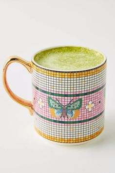 a cup with a butterfly painted on the side and gold trim around the edge, sitting on a white surface