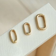 three pairs of gold - plated metal rings on a white surface, with one ring in the middle