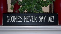 there is a sign that says goonies never say die next to a potted plant