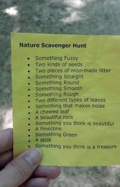 a hand holding a yellow post it note with words on it that say nature scavenger hunt