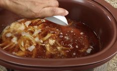 a person using a spoon to stir noodles in a crock pot