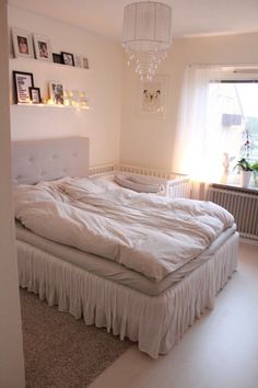 an unmade bed in a white bedroom with pictures on the wall above it and a chandelier hanging from the ceiling