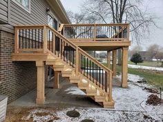 a wooden stair case next to a brick building with snow on the ground and trees in the background