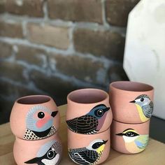 four vases with birds painted on them sitting on a table next to a brick wall