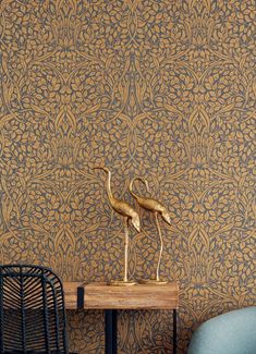 two gold flamingos are on a small table in front of a wallpapered room