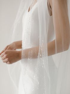 a woman wearing a white veil and holding her hand under the veil with water droplets on it