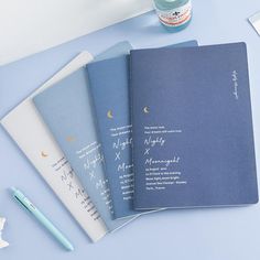 three blue notebooks with writing on them next to a cup of coffee and a pen