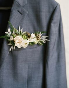 a man in a gray suit with white flowers on his lapel and green leaves