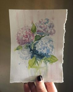 a person holding up a piece of paper with watercolor flowers in it