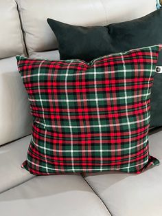 a plaid pillow on a white couch with black and red pillows in the corner,